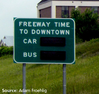 Photo of a signs designed to display travel time differences between private vehicle (car) and public transit (bus).