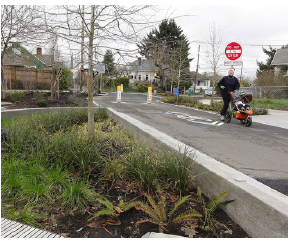 An approach to a signalized intersection on a two lane road. A dedicated bike lane is painted solid green and the stop bar is placed several feet back from the corner. The green bike lane extends from the curbside across to the double yellow line, giving bicyclists using the road a visible place in front of stopped traffic.