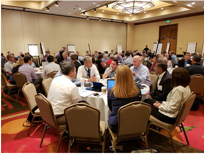 Image of ballroom with multiple groups of peoples sitting around round tables.