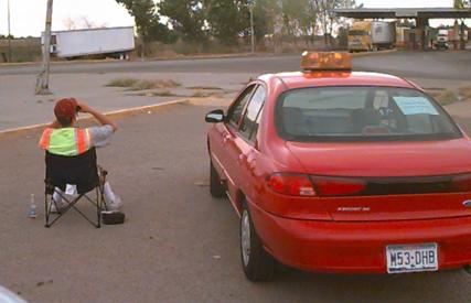 Photo of Inbound 1 data collection point at initial gate on Mexican side, with an official sitting next to his car in the foreground watching trucks at the gate.