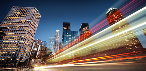 Blurred fast moving cars on road against city skyline at night