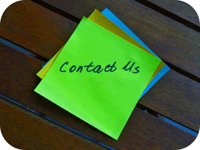 Bright green sticky note on a wooden surface with "contact us" written on it using a dark marker.