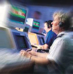 Photo. People wearing headsets while at work on computers as part of back-office operations at a monitoring station.