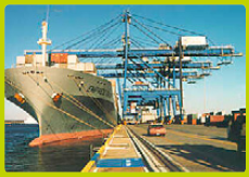 Photo of a container ship moored alongside a pier where the cargo may be removed by nearby cranes.