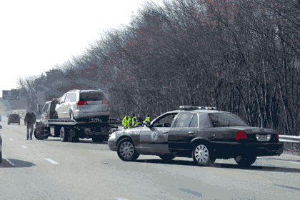 Picture of a police car blocking part of a road and a police officer addressing a problem with a tractor trailer.