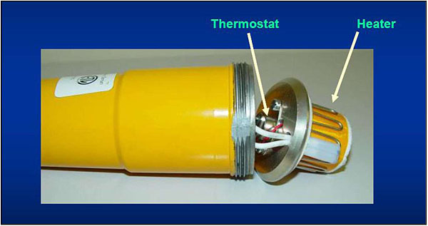 Figure 8. FAA LED Heating Element (E. Runyon). In this photograph, there is a yellow cylinder with a white label partially showing on its top side to the left of the photograph. The cylinder has been opened on the right side. Metal grooves are visible on the outer rim of the cylinder; wires and metal elements are visible on the interior, underneath side of the top of the cylinder. On the other side of the top of the cylinder is a series of weaving metal coils around a yellow round cylinder with a white rim at the end. There is an arrow and the word Heater pointing to the weaving coils. There is an arrow pointing to the wires and metal elements inside the cylinder with the word Thermostat.