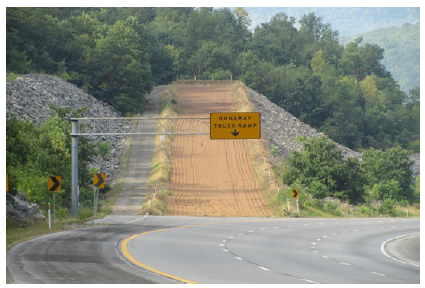 A runaway truck ramp on a roadway through a mountainous area with winding roads.