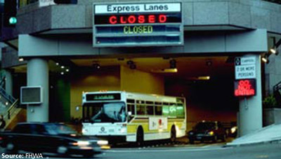 Photo of multiple lanes of traffic emerging from a tunnel which can alternately be used to allow express lane traffic to flow in the other direction. Above the tunnel is a large sign indicating the tunnel is closed to express lane traffic in that direction.