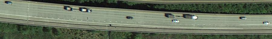 Aerial photo of a shoulder lane on a highway in Washington State. The inside edge of the shoulder lane changes from a solid white line to a dashed white line at the point where vehicles in the adjacent travel lane are permitted to begin merging into the shoulder lane towards the downstream exit ramp. The inside edge line of the shoulder lane returns to solid white after vehicles from the adjacent travel lane are no longer allowed to switch lanes to exit at the downstream ramp.