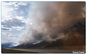 Aerial photo of a road running near the base of a mountain where the side of the mountain is on fire and billowing smoke. Source: Fotolia