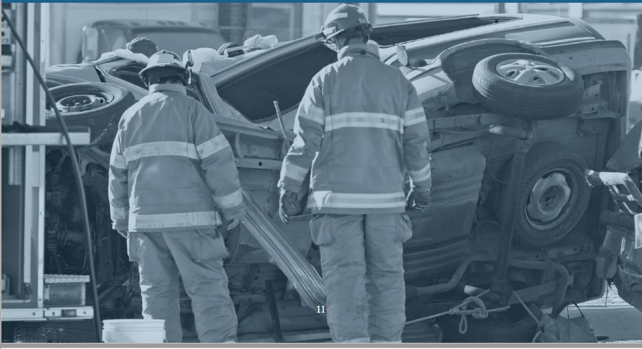 Two fireman look at a crashed car on it's side.