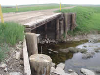 Small brige on dirt road with no rails with a small stream under it.