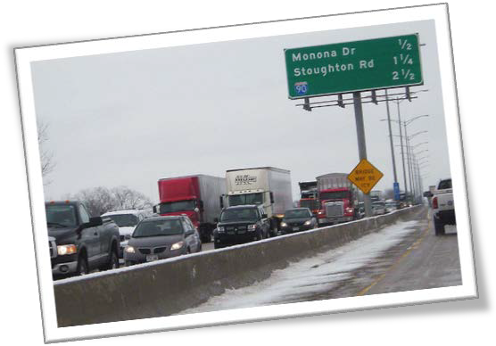 This picture shows cars and trucks in traffic on a highway with snow.