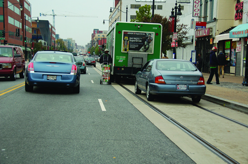 Green soft drink delivery truck with driver unloading truck that is parked on top of streetcar tracks on D.C. street.