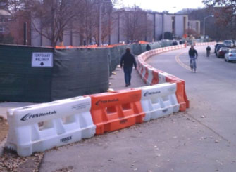 This photo shows longitudinal channelizing devices arranged to delineate a pedestrian walkway on the far left side of a street.