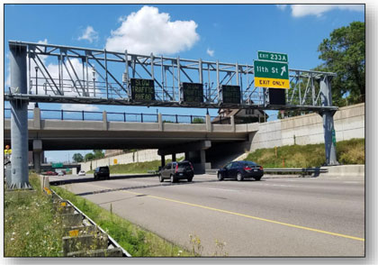 Photograph of an overhead sign gantry with dynamic lane control signs over each lane.  The signs read 'SLOW TRAFFIC AHEAD.'