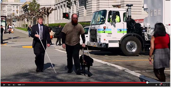 Scene from the SMFTA large vehicle driver safety awareness video shows a large vehicle stopped at an intersection while pedestrians cross the street