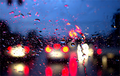 Windshield with rain drops and blurred night time view of car tail lights.