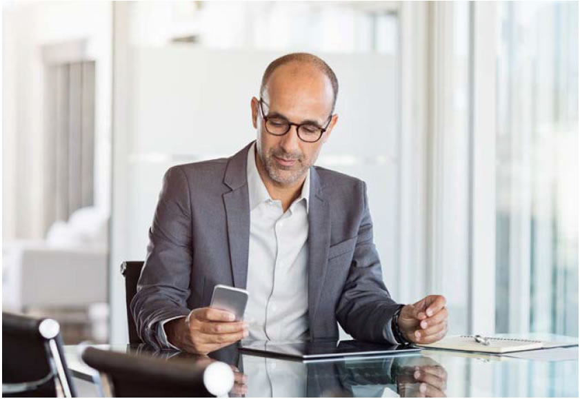 The image is of a man at his desk looking at his cellphone.