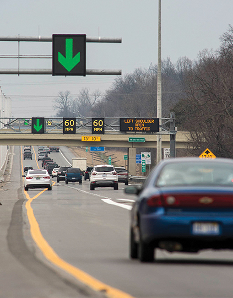 Roadway with overhead stanchions showing variable speed limits and green lane open arrows.