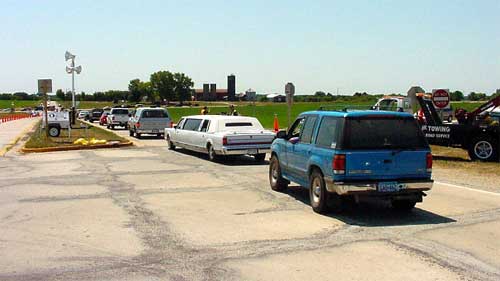 traffic traversing a venue access road and monitored by two field personnel with a tow truck stationed on the right shoulder and a portable lighting device positioned in the access road median