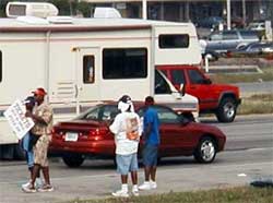 photo showing a group of pedestrians standing on a roadway shoulder holding a sign stating "tickets – buy and sell – pull in"