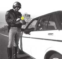 Photograph - Police officer standing near the driver's side door of an automobile.  The Police officer is writing a citation.