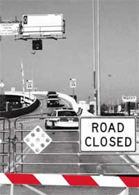 Photograph:  An HOV ramp that has been closed.  In the foreground, temporary barriers have been deployed with signs that read ROAD CLOSED.  The ramp also has two permanent swing gates (one in the foreground and one in the background).  The swing gate in the foreground has been lowered, closing the ramp to all traffic.