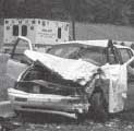 Photograph - Damaged vehicle with ambulance in the background.  Damage to the vehicle is contained to the front of the vehicle.