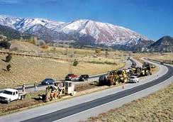 photograph of a construction site, with many vehicles and trench digging machines laying cable next to a roadway