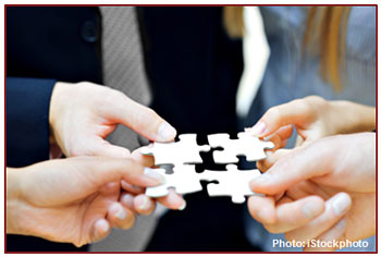 Photo of four hands holding four puzzle pieces.