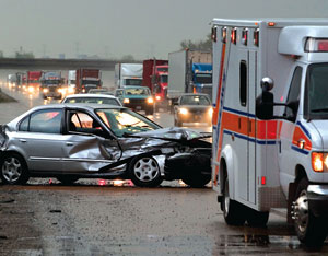 Photo of a car with a smashed front end on the side of the road behind an emergency response vehicle.