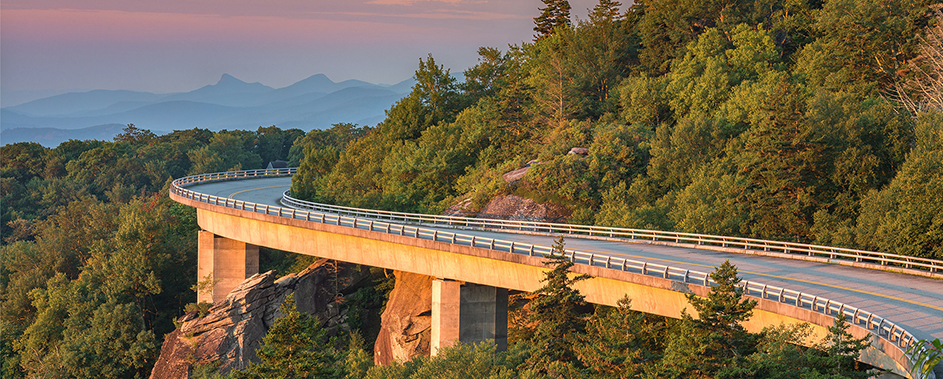 a highway curving around the side of a forested mountain