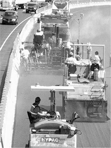 Figure 3 - Nearly 80 million pounds of asphalt were delivered in less than 100 hours. The picture shows a line of four construction machines preparing the roadway for applications of asphalt.