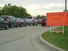 A horizontal orange sign displayed on side of road with the wording ROAD WORK AHEAD EXPECT DELAYS.