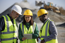 People in construction hard hats look at computer tablet.