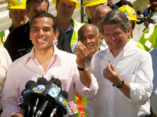 Two men standing behind a bank of microphones holding up chips of concrete for the cameras.