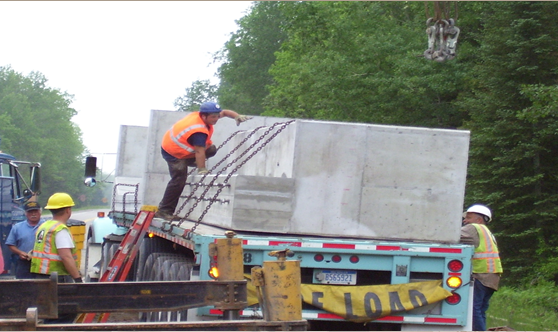 Workers loosening the chains securing a Hy-Span bridge to the back of the flatbed that was used to transport it to the job site.