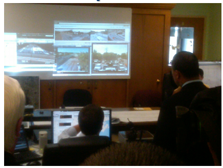 A large video screen with staff working on laptops in the command center.