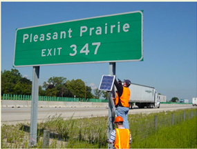 Two workers installing a detector onto a roadside sign.