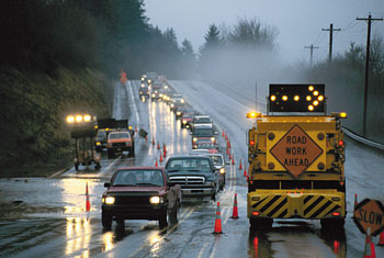 Photo of an advance warning arrow board and Road Work Ahead caution sign on a work vehicle next to a lane of traffic.