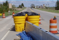 Photo of a set of yellow impact attenuator barrels surrounding the terminus of a jersey wall used to separate the throughway from a closed shoulder.