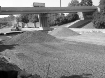 Figure 1 shows a segment of roadway under full closure. Base aggregate is being dumped on the roadway in preparation for paving.  A bridge which extends over the fully closed roadway is also closed to traffic.