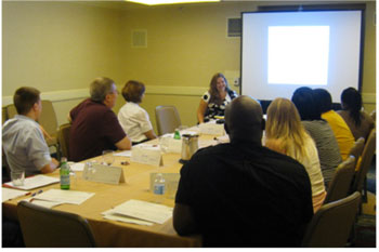 A photo shows a group of people around a table facing a presentation screen.