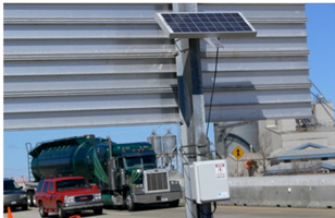 A roadside bluetooth detector mounted at the rear of a post-mounted roadway sign.