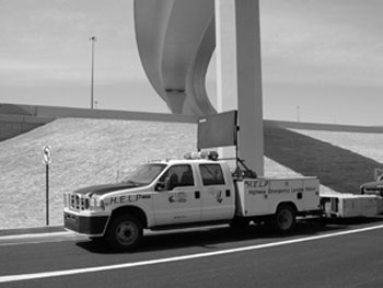 Figure 2 - This figure shows a highway emergency lender patrol vehicle with a mounted arrowboard and crash cushion sitting under an overpass. The vehicle is a truck with flashing lights and is used to assist motorists.